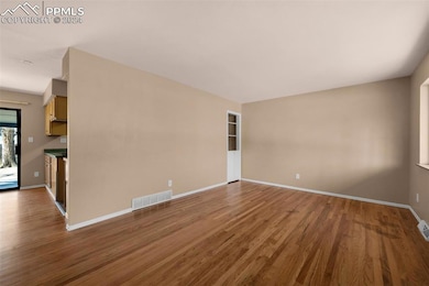 Living room with hard wood flooring looking into kitchen nook and kitchen.