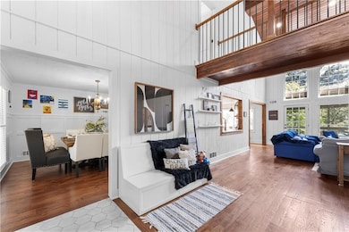 Living area with a towering ceiling, a decorative wall, a chandelier, wood finished floors, and crown molding