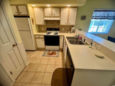 Kitchen featuring range with electric stovetop, freestanding refrigerator, under cabinet range hood, a sink, and light countertops