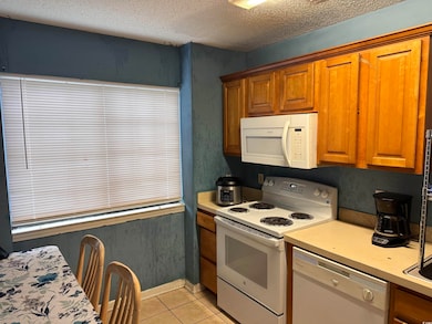 Kitchen with white appliances, light tile patterned floors, brown cabinets, light countertops, and a textured ceiling