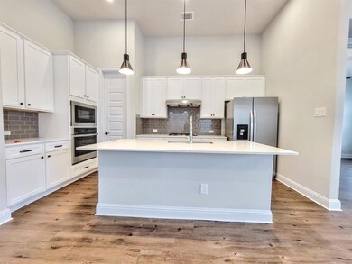 Kitchen featuring white cabinets, hanging light fixtures, appliances with stainless steel finishes, tasteful backsplash, and light wood-style floors