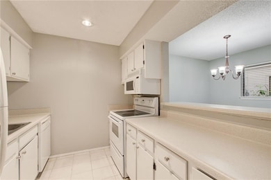 Kitchen featuring baseboards, light countertops, white appliances, and white cabinets
