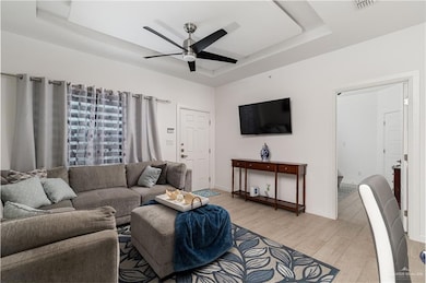Living room with light wood finished floors, a ceiling fan, baseboards, a tray ceiling, and visible vents