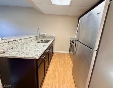 Kitchen featuring light stone counters, appliances with stainless steel finishes, a drop ceiling, a peninsula, and light wood finished floors