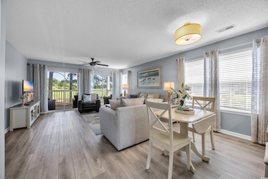 Living area featuring a textured ceiling, ceiling fan, light wood finished floors, and baseboards