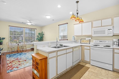 Kitchen featuring white appliances, a peninsula, light countertops, ceiling fan, and white cabinetry