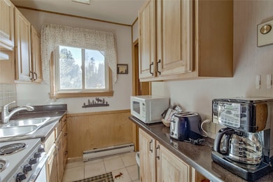 Kitchen featuring light brown cabinetry, crown molding, baseboard heating, sink, and white appliances
