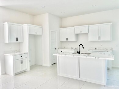 Kitchen with sink, white cabinets, light stone countertops, and a center island with sink