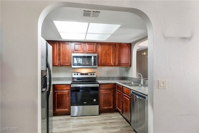 Kitchen featuring appliances with stainless steel finishes, arched walkways, light wood-type flooring, and a textured wall