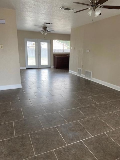 Unfurnished living room featuring a ceiling fan, a textured ceiling, and dark tile patterned flooring