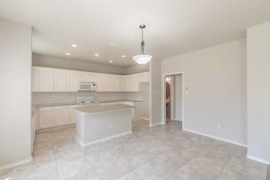 Kitchen featuring tasteful backsplash, decorative light fixtures, light stone counters, white appliances, and white cabinets