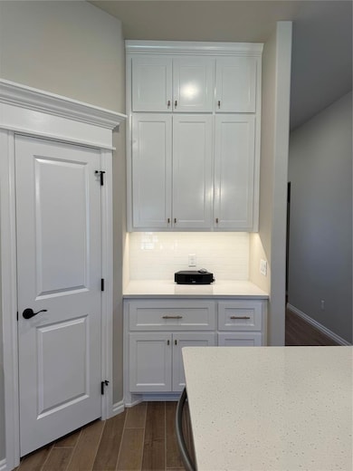 Kitchen featuring wood finish floors, white cabinetry, light stone counters, and backsplash