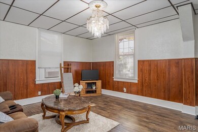 Main floor Living room featuring wooden walls, a wainscoted wall, wood finished floors, a paneled ceiling, and a chandelier
