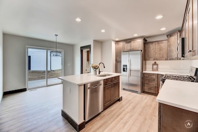Kitchen with appliances with stainless steel finishes, an island with sink, decorative light fixtures, light wood-type flooring, and recessed lighting