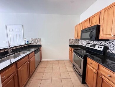 Kitchen with stainless steel appliances, backsplash, light tile patterned flooring, dark stone counters, and brown cabinetry