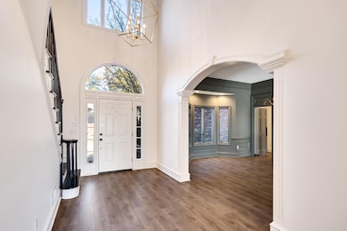 Foyer with plenty of natural light, arched walkways, wood finished floors, a chandelier, and a towering ceiling