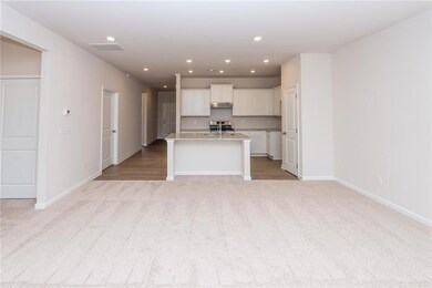 Kitchen with stainless steel gas range oven, under cabinet range hood, white cabinets, light colored carpet, and a center island with sink