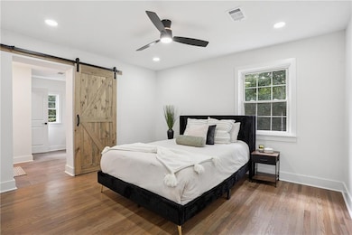 Bedroom with wood finished floors, a ceiling fan, recessed lighting, and a barn door