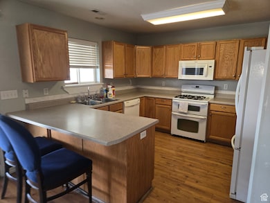 Kitchen featuring white appliances, a peninsula, dark wood-style flooring, a breakfast bar, and brown cabinetry