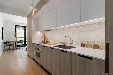 Kitchen with modern cabinets, backsplash, light wood-style floors, and light stone countertops