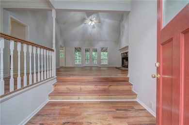 Stairs with high vaulted ceiling, wood finished floors, a ceiling fan, baseboards, and a fireplace with raised hearth