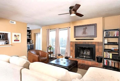 Living room with a textured ceiling, wood finished floors, a fireplace with raised hearth, and ceiling fan