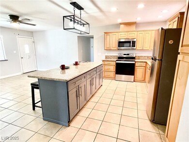 Kitchen featuring stainless steel appliances, light tile patterned floors, pendant lighting, a breakfast bar area, and light stone counters