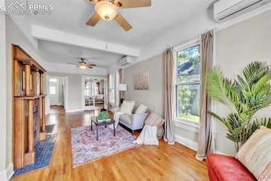 Living area featuring an AC wall unit, a ceiling fan, wood finished floors, and beamed ceiling