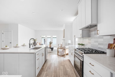 kitchen featuring stainless steel appliances, backsplash, light wood finished floors, white cabinetry, and light stone counters