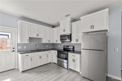 Kitchen with stainless steel appliances, a sink, white cabinetry, tasteful backsplash, and dark countertops