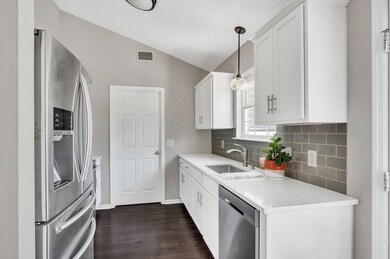 The galley style kitchen features white painted cabinets, quartz countertops, stainless steel appliances, updated lighting, large stainless steel sink with window overlooking the back yard, and ceramic tile backsplash.