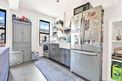 Kitchen with stainless steel appliances, gray cabinets, open shelves, and light tile patterned flooring