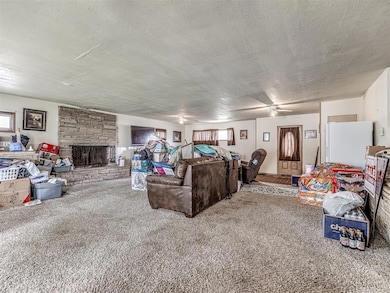 Living area featuring a textured ceiling, carpet floors, a stone fireplace, and ceiling fan
