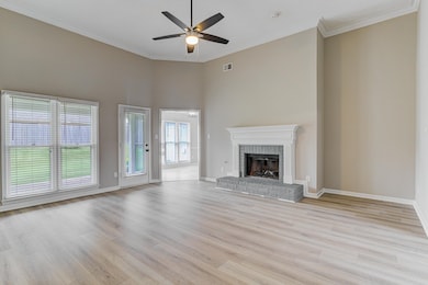 Unfurnished living room with ceiling fan, light wood-type flooring, a fireplace, baseboards, and ornamental molding