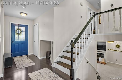Entrance foyer featuring a glass covered fireplace, dark wood finished floors, and stairway