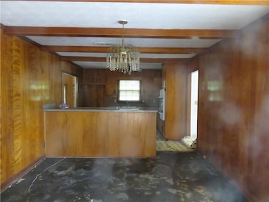 Kitchen featuring a peninsula, wooden walls, a chandelier, beamed ceiling, and brown cabinetry