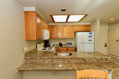 Kitchen with a kitchen bar, a peninsula, white appliances, light stone counters, and recessed lighting
