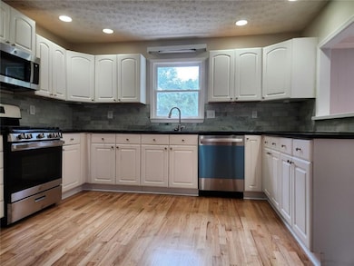 Kitchen with appliances with stainless steel finishes, a textured ceiling, dark countertops, white cabinetry, and recessed lighting