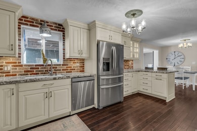 Kitchen with a peninsula, stainless steel appliances, light stone counters, decorative light fixtures, and a textured ceiling