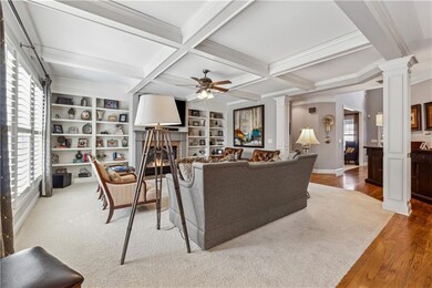 Living area with decorative columns, wood finished floors, ceiling fan, ornamental molding, and a glass covered fireplace
