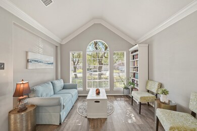This formal sitting area is bright and inviting, showcasing elegant design and natural warmth. A soaring vaulted ceiling with crisp crown molding adds height and visual interest, while the large arched window framed by double side windows fills the space with natural light. The layout offers a perfect balance of style and function.