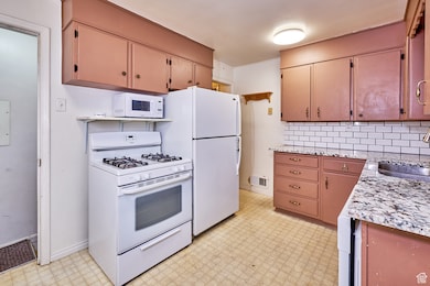 Kitchen featuring light floors, white appliances, and backsplash