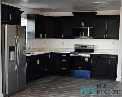 Kitchen with dark cabinets, stainless steel appliances, and wood finish floors
