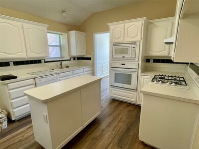 Kitchen with backsplash, white cabinets, a kitchen island, light countertops, and white appliances