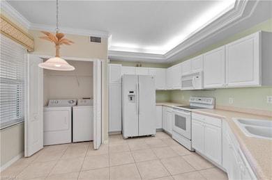 Kitchen featuring white appliances, light countertops, decorative light fixtures, white cabinetry, and light tile flooring
