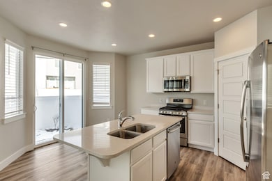 Kitchen with white cabinetry, appliances with stainless steel finishes, light wood finished floors, a kitchen island with sink, and recessed lighting