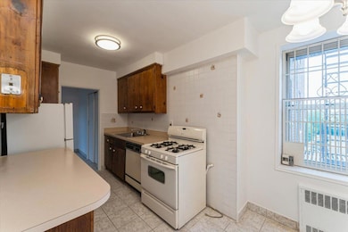 Kitchen featuring white appliances, radiator heating unit, a sink, light countertops, and light tile patterned flooring