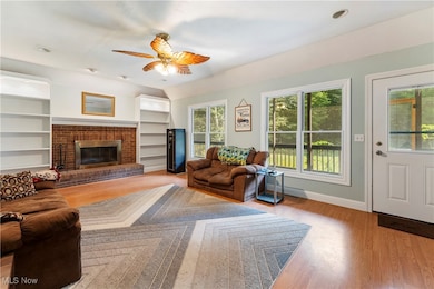 Living area with light wood-type flooring, a fireplace, ceiling fan, and built in shelves