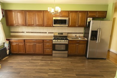 Kitchen featuring stainless steel appliances, a chandelier, decorative backsplash, dark wood-type flooring, and hanging light fixtures