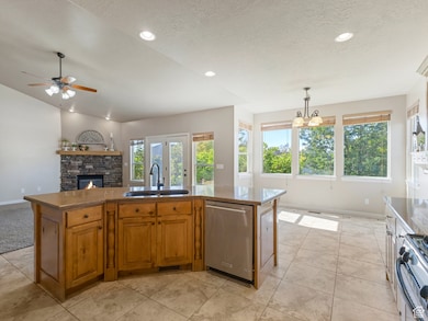 Kitchen featuring brown cabinets, a stone fireplace, stainless steel appliances, open floor plan, and an island with sink